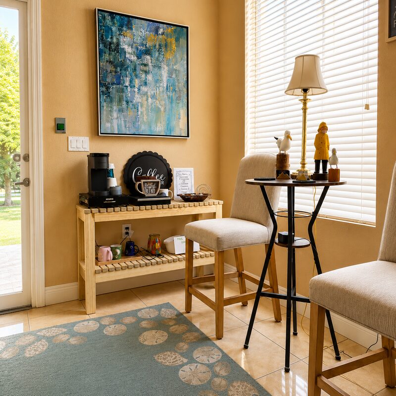 Coffee station beside a blue abstract painting and a sunlit window with a sand-dollar rug