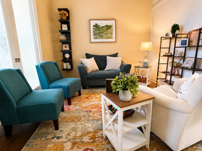 Warm, inviting therapy room with teal accent chairs and a comfortable loveseat at Living Well Counseling & Consulting