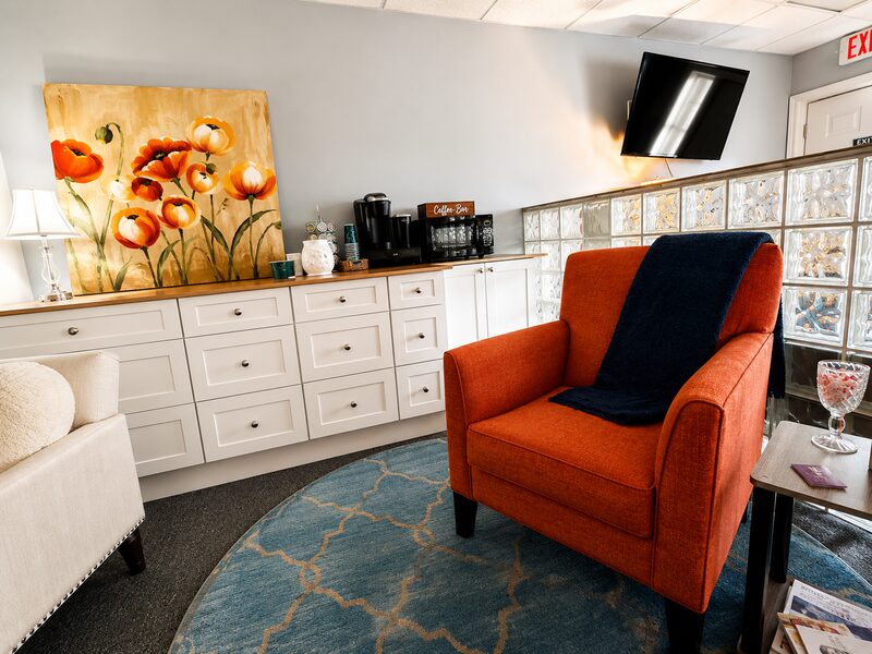Waiting lounge with a bright orange armchair, a poppy painting, and a coffee station