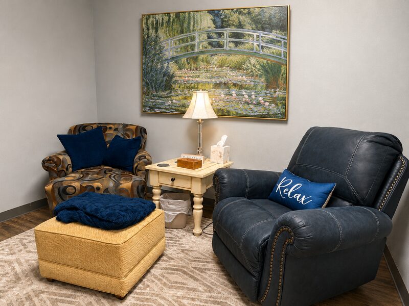Therapy room with a navy leather recliner, a 'Relax' pillow, and a Monet water-lilies painting